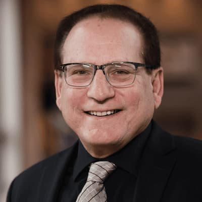 Man with glasses in dark suit and silver tie. 