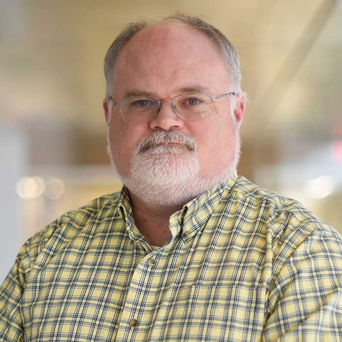 Man with glasses and beard, wearing green plain dress shirt. 