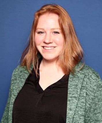 Smiling woman with red hair, in black shirt with green sweater.